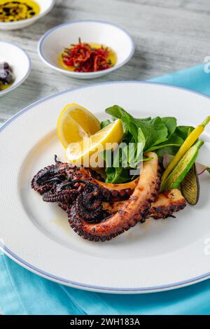 Polpo grigliato con rucola e mini verdure su un piatto di porcellana bianca Foto Stock