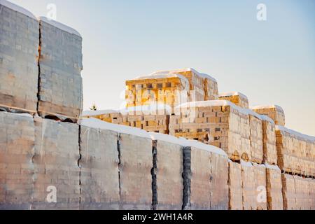 Mattoni su pallet imballati o avvolti con plastica impilata con resti di neve sulla superficie superiore, contro il cielo blu nelle soleggiate giornate invernali nei Paesi Bassi. Foto Stock