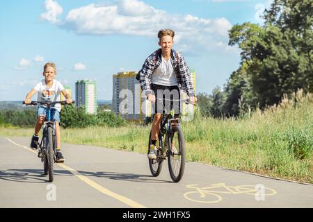 Due ragazzi stanno andando in bicicletta su una pista ciclabile nel parco. Indossano entrambi abiti informali e sembrano godersi il clima caldo Foto Stock