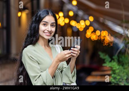 Una giovane donna indiana irradia di gioia mentre esplori le strade della città, smartphone in mano, combinando perfettamente turismo e tecnologia. Foto Stock