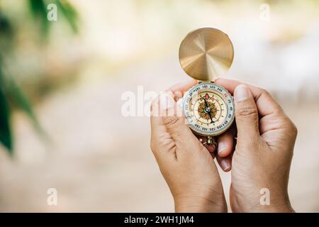 La mano di una donna tiene una bussola in un primo piano mentre cammina nella foresta. La bussola simboleggia Foto Stock