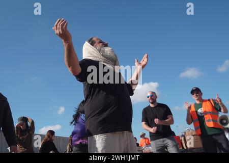 I manifestanti israeliani di destra ballano bloccando i camion egiziani che trasportano aiuti umanitari nella Striscia di Gaza sul lato israeliano dell'attraversamento di Karem Abu Salem, noto anche come attraversamento di Kerem Shalom il 6 febbraio 2024 a Kerem Shalom, Israele. Da diversi giorni ormai, i coloni israeliani bloccano i camion che trasportano rifornimenti umanitari ai palestinesi nella Striscia di Gaza assediata. Foto Stock