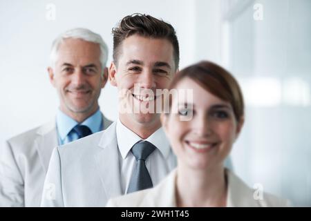 Sorridente, un gruppo cordiale di tre uomini d'affari, e di personale di compagnia privata di diversa età che posa per ritratti d'ufficio. Partner commerciali diversi Foto Stock