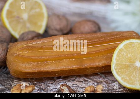 Torta dolce turca chiamata tulumba, servita al piatto con fette di limone e noci intorno, su un enorme tavolo di legno Foto Stock
