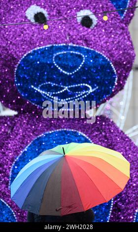 Dresda, Germania. 7 febbraio 2024. Una donna si erge con un ombrello colorato di fronte a un orsacchiotto oversize, che è una decorazione al Festival invernale di Dresda sull'Altmarkt. Crediti: Robert Michael/dpa/Alamy Live News Foto Stock