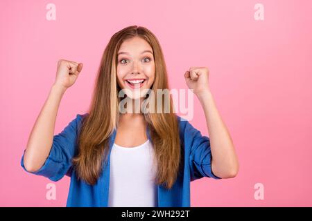 Foto di una ragazza fortunata che indossa camicia blu braccia guance pugni che urlano sì spazio vuoto sfondo rosa isolato Foto Stock