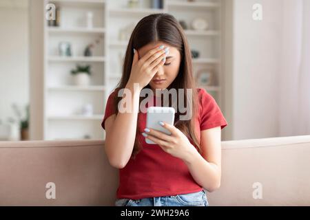 Cattive notizie. Turbare la donna asiatica toccando la testa dopo aver letto il messaggio sullo smartphone Foto Stock