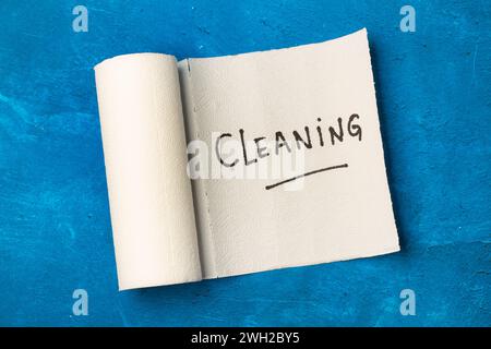 Parola per la pulizia scrivere su un rotolo di carta da cucina su uno sfondo blu con vista dall'alto Foto Stock