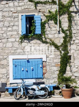 Un ciclomotore blu parcheggiato di fronte ad un antico edificio in pietra Foto Stock