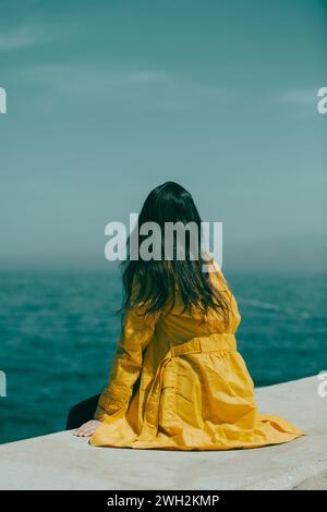 Una donna con l'impermeabile giallo sedeva sulla spiaggia Foto Stock