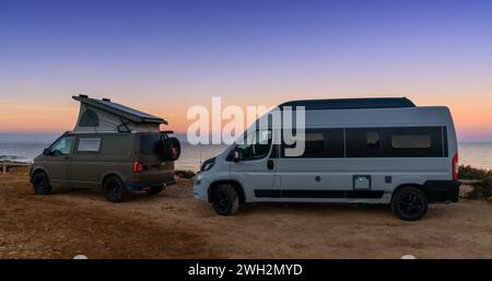 Santa Pola, Spagna - 4 febbraio 2024: Due camper parcheggiati in un parcheggio di sabbia accanto alla spiaggia al tramonto Foto Stock