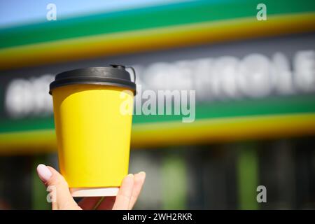 Una femmina tiene una tazza di carta di cartone giallo con coperchio nero per bevande calde. Tè in mano a una donna. Mockup all'aperto. Tazze da portare via per il caffè Foto Stock