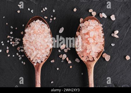 Due cucchiai di legno adagiati su un'ardesia sono riempiti di sale rosa Foto Stock