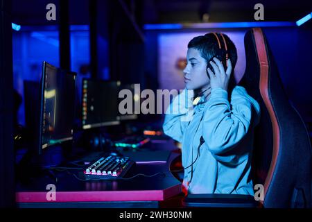 giovane donna concentrata che indossa le cuffie mentre gioca in una stanza illuminata dal blu, cybersport Foto Stock