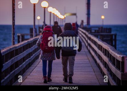 Wustrow, Germania. 7 febbraio 2024. I turisti si dirigono al molo dopo il tramonto. Con temperature fredde di circa tre gradi e venti forti, il clima nel nord della Germania mostra il suo lato ventoso. Crediti: Jens Büttner/dpa/Alamy Live News Foto Stock