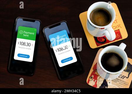 Due smartphone sul tavolo che mostrano l'invio e la ricezione di pagamenti tramite l'app portafoglio digitale su un telefono cellulare. Ci sono un paio di tazze di caffè nero Foto Stock