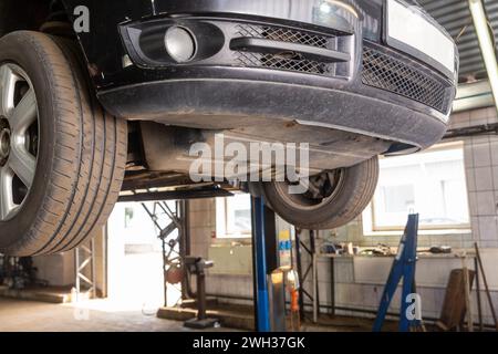 Auto sollevata su un ascensore in autoservice. Vista dal basso di un'auto su un sollevatore presso l'officina meccanica. Foto Stock