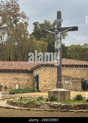 Santa Barbara, CA, USA - 18 dicembre 2023: Primo piano della statua di Gesù sulla Croce nel cimitero della chiesa della Vecchia missione. Pietre e croci di tombe storiche Foto Stock