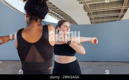 Due donne più grandi in un abbigliamento fitness nero per riscaldarsi. Le giovani donne allungano le mani sotto un ponte. Foto Stock