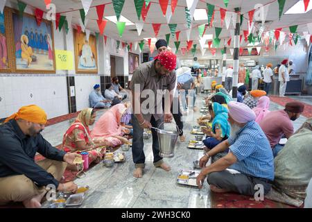 Uomini e donne mangiano un pasto vegetariano in un langar in un tempio Sikh nel Queens, New York. A Langars, a tutti e a tutti viene offerto un pasto gratuito. Foto Stock