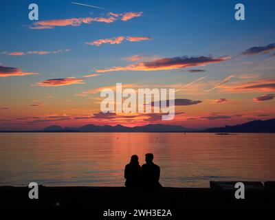 Romantico tramonto sulla baia di Cannes, Riviera, Francia, con una giovane coppia seduta e sagomata sul mare rosa. Foto Stock