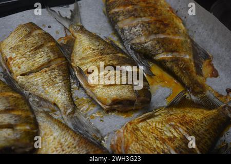 Pesce delizioso e sano, al forno, Carassius con limone su una teglia nera da forno con carta bianca pergamena. Foto Stock