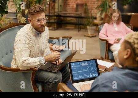 Ritratto di un uomo barbuto che indossa gli occhiali mentre parla con il collega e collabora al progetto in uno spazio di coworking vintage Foto Stock