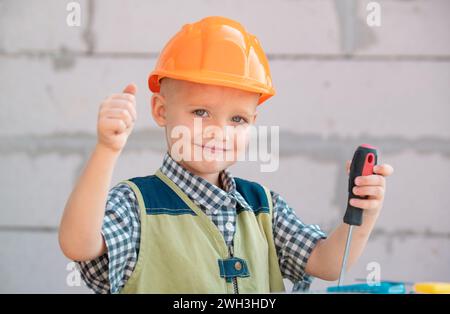 Bambino in casco protettivo arancione con strumenti per la ristrutturazione. Sorridente felice bambini costruttore e riparazione. Foto Stock