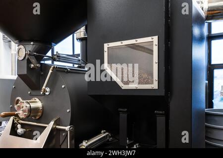 Foto ravvicinata della torrefazione industriale nera, i semi di caffè tostati sono dietro la finestra tecnologica Foto Stock