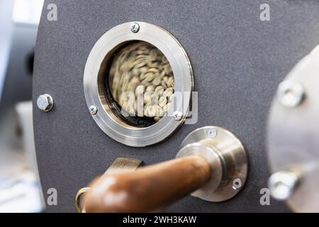 Foto ravvicinata della torrefazione industriale, semi verdi si trovano all'interno dietro una piccola finestra tecnologica rotonda Foto Stock