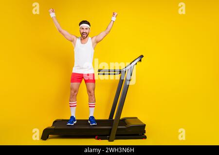 Foto a figura intera del bellissimo e felice tapis roulant alzare i pugni di successo spazio vuoto isolato su sfondo giallo Foto Stock
