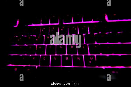 Tastiera per PC da gioco di colore rosa illuminato e sfondo nero scuro Foto Stock