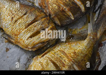 Pesce delizioso e sano, al forno, Carassius con limone su una teglia nera da forno con carta bianca pergamena. Foto Stock