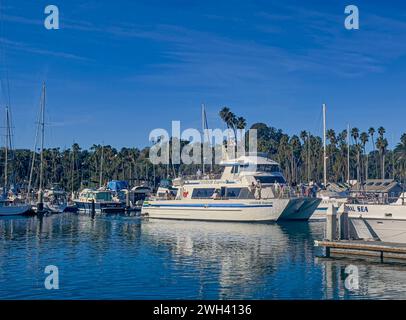 Santa Barbara, CA, USA - 28 gennaio 2024: Primo piano dell'escursione in barca turistica Condor Express che naviga nel porto. Molta gente sul ponte, verde fogliame Foto Stock