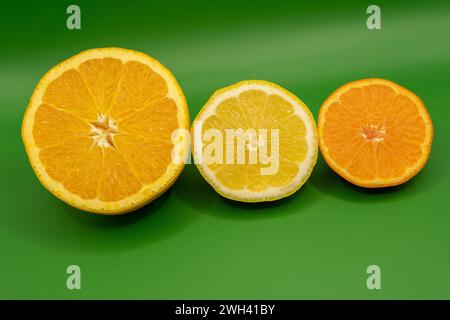 Metà arancio, limone e mandarino su sfondo verde Foto Stock