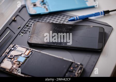 Primo piano di uno smartphone con touch screen rotto visualizzato sul tavolo nell'officina di riparazione elettronica Foto Stock