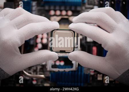 Tecnico non riconoscibile tenendo con cura la CPU con le dita prima di inserirla nella scheda madre del PC Foto Stock
