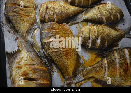 Pesce delizioso e sano, al forno, Carassius con limone su una teglia nera da forno con carta bianca pergamena. Foto Stock