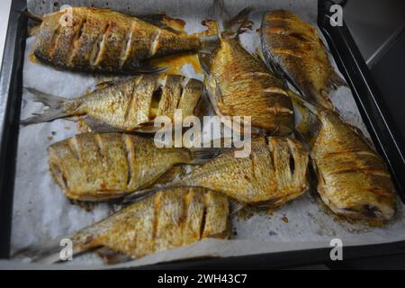 Pesce delizioso e sano, al forno, Carassius con limone su una teglia nera da forno con carta bianca pergamena. Foto Stock