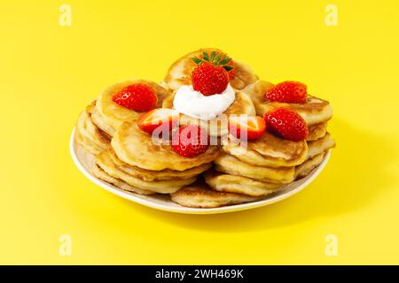Mini pancake con fragole e panna acida su sfondo giallo Foto Stock