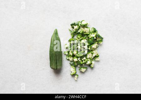 Vista dall'alto dell'okra su uno sfondo bianco, le dita di una signora su un ripiano di marmo, okro preparato per cucinare Foto Stock