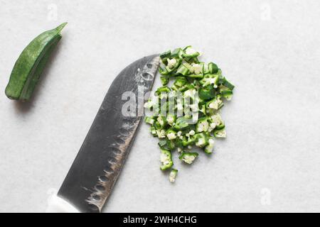 Vista dall'alto dell'okra su uno sfondo bianco, le dita di una signora su un ripiano di marmo, okro preparato per cucinare Foto Stock