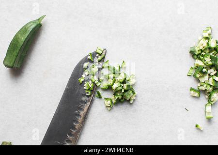 Vista dall'alto dell'okra su uno sfondo bianco, le dita di una signora su un ripiano di marmo, okro preparato per cucinare Foto Stock