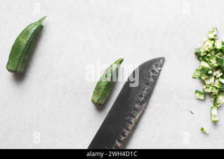 Vista dall'alto dell'okra su uno sfondo bianco, le dita di una signora su un ripiano di marmo, okro preparato per cucinare Foto Stock