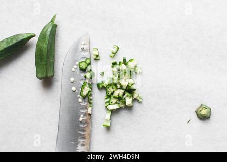 Vista dall'alto dell'okra su uno sfondo bianco, le dita di una signora su un ripiano di marmo, okro preparato per cucinare Foto Stock