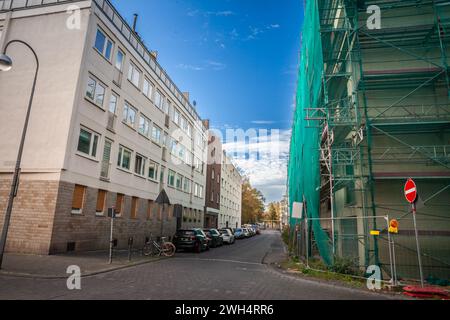 Immagine di un quartiere residenziale di Colonia, in Germania, con auto parcheggiate in una strada deserta, edifici a più piani e progetti di ristrutturazione in corso Foto Stock