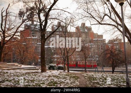 Foto di un tram che passa accanto a un parco innevato di Banjica in inverno. Banjica è un'area residenziale situata nel comune di Savski Venac di Belgrado, Th Foto Stock