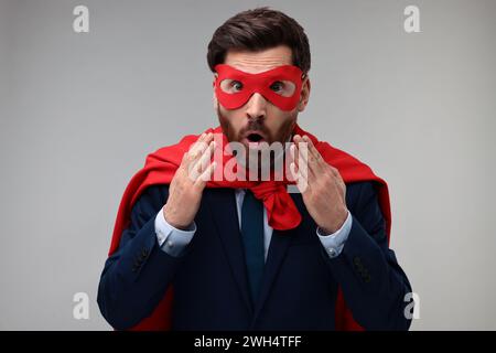 Uomo d'affari sorpreso con mantello rosso supereroe e maschera su sfondo beige Foto Stock