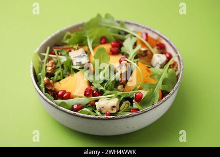 Gustosa insalata con cachi, formaggio blu, melograno e noci serviti su sfondo verde chiaro Foto Stock