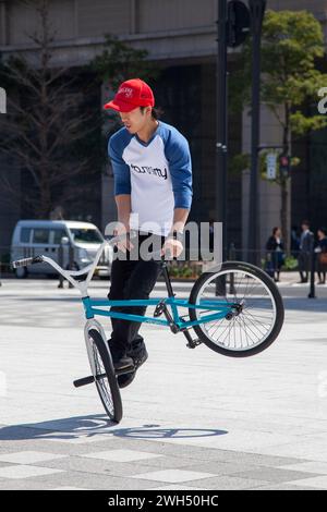 Un pilota giapponese BMX esegue trucchi in una piazza pubblica nel mezzo dell'area commerciale di Tokyo, in Giappone. Foto Stock